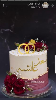 two wedding rings on top of a cake with red roses and greenery in the foreground