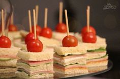 small sandwiches with meat, cheese and tomatos on toothpicks are arranged on a glass platter