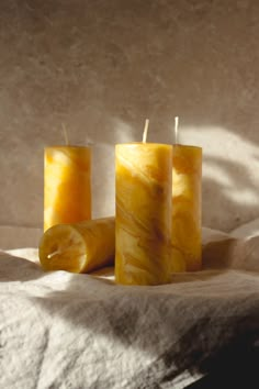 three yellow candles sitting on top of a bed next to each other with one candle in the middle