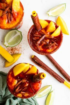 two glasses filled with fruit and cinnamon on top of a white table next to sliced limes