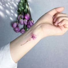 a woman's arm with a small pink flower tattoo on the left side of her wrist