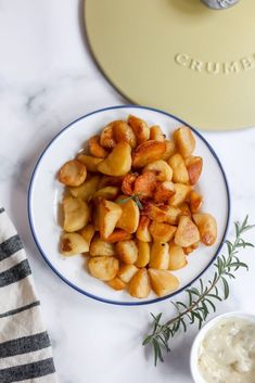 a white plate topped with potatoes next to a bowl of ranch dressing on top of a marble counter