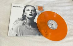 an orange vinyl record sitting on top of a white bed next to a magazine cover