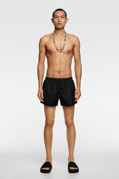 a man in black swim trunks standing with his shirt off