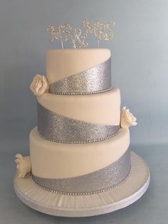 a three tiered wedding cake with silver and white frosting, roses and monograms on top