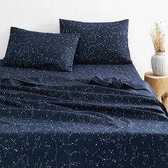 a bed with blue sheets and stars on it, next to a vase filled with dried flowers