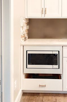 a white microwave oven sitting inside of a kitchen next to cupboards and drawers on the wall