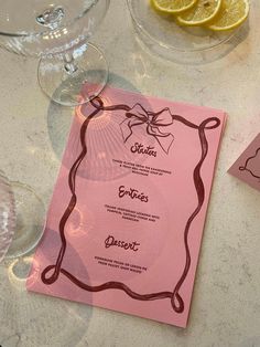 a pink menu sitting on top of a table next to wine glasses and lemon wedges