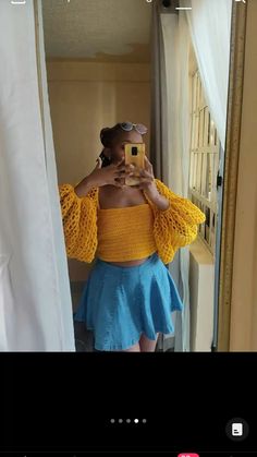 a woman taking a selfie in front of a mirror wearing a yellow top and blue skirt