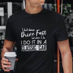 a man holding a coffee cup and wearing a black t - shirt that says i don't always drive fast but when i do, i do it in a classic car