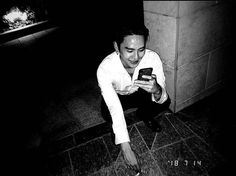 a man in white shirt and black pants looking at cellphone while kneeling on the ground