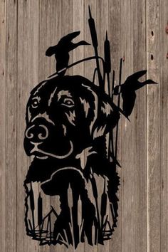 a black dog is standing in front of a fence with reeds and birds on it