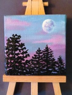 an easel with a painting on it that has trees and the moon in the sky