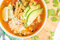 a bowl of mexican soup with avocado, cilantro, and rice