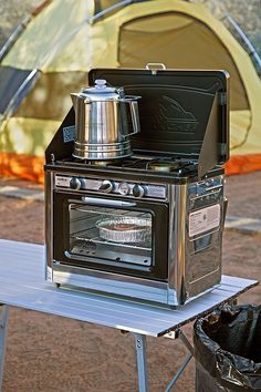 an oven on a table in front of a tent with a stove and pot on top