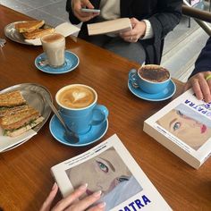 people sitting at a table with coffee, sandwiches and magazines on the table in front of them