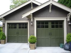 two garages with green doors and plants in pots on the side of the building