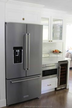 a stainless steel refrigerator and freezer combo in a kitchen with hardwood flooring, white walls and cabinets