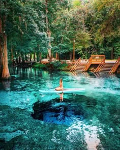 a person on a surfboard in the middle of a lake surrounded by trees and stairs