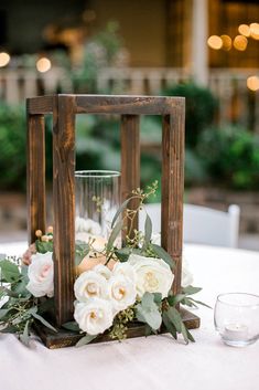 a wooden lantern with flowers and greenery sits on top of a table at a wedding reception