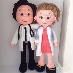 two crocheted dolls standing next to each other in front of a white wall