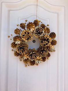 a wreath made out of pine cones hanging from a door handle on a white door