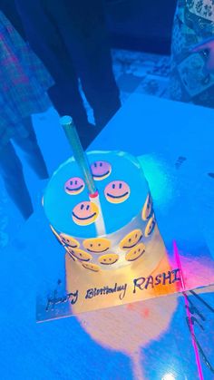 a blue cake with smiley faces on it sitting on top of a table next to people