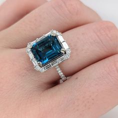 This beautiful art deco ring features a vibrant London blue topaz set in 14k white gold with roudnd and baguette diamond accents. A statement ring design perfect for an eye catching engagement or anniversary. This ring also makes a beautiful birthstone ring for your loved ones. The occasions to show off this ring are endless - mother's day, graduation, wedding, birthday, date night, Christmas, etc. :) Item Type: Ring Stone: London Blue Topaz Weight: 5.4cts Cut: Faceted Shape: Emerald Cut Head size: 11x9mm Metal 14k/4.02g Diamonds S/I GH: 32/0.84cts Sku:AJR252/3458 Our piece can be made... - In dual tone, 18k gold, or platinum - To fit your gem's unique size and shape - With higher color and clarity of diamonds - As bezel set, prong set, etc. - To stack with your bands - With different gem Luxury Art Deco Topaz Ring With Prong Setting, Blue Topaz Ring In Platinum, Blue Topaz Ring With Prong Setting In Platinum, Gia Certified Blue Art Deco Jewelry, Blue Art Deco Jewelry Gia Certified, Platinum Blue Topaz Ring With Center Stone, Blue Topaz Platinum Ring With Halo Setting, Blue Topaz Ring With Accent Stones In Platinum, Art Deco Blue Asscher Cut Ring