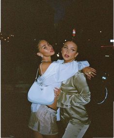 two women standing next to each other in front of a dark sky with lights on