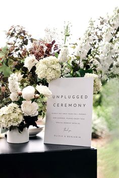 white flowers and greenery are arranged in vases on a table with a menu