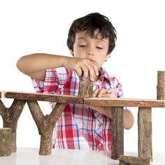 a young boy sitting at a wooden bench made out of branches and logs with one hand on the table