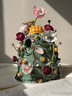 a green cake with flowers on it sitting on top of a white sheet covered table