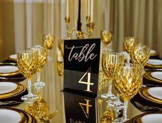 a table set up for a formal dinner with gold and black plates, silverware, and place cards