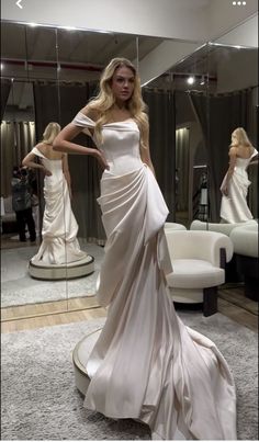 a woman standing in front of a mirror wearing a white dress and posing for the camera