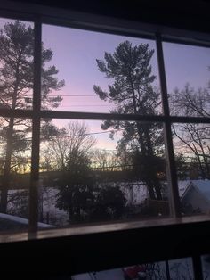 the sun is setting over some trees and houses from a window sill in front of a snow covered yard