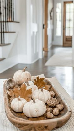 a wooden bowl filled with white pumpkins and nuts on top of a table next to stairs