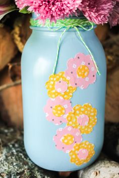 a blue mason jar with pink flowers in it and string tied around the top, sitting on rocks