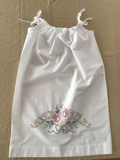 This is a beautiful white cotton/polyester "pillowcase" dress created by Mary that will fit children ages 3 through 8 years old.  It has been created from a brand new 20 x 30-inch white pillowcase that is 60% cotton and 40% polyester.  Mary has carefully and meticulously hand-embroidered the beautiful pastel "Floral Swag" design on the front of the dress using 100% cotton embroidery floss.  The embroidered design measures approximately 12 inches wide x 6 inches tall.  The ribbon straps are adjustable and gather gently around the neckline.  You have the option of white, green, or pink ribbon straps subject to availability.  I currently have one of each color in stock.  Please choose which color you prefer at checkout.   What a beautiful summertime or Easter dress for your child or grandchil White Cotton Dress With Machine Embroidery, Hand Embroidered Dress, Swag Design, Girls Spring Dresses, Girls White Dress, Floral Swag, Pillowcase Dress, School Dresses, Embroidered Pillowcases