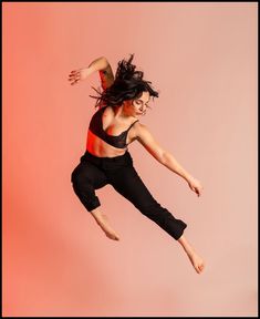 a woman jumping in the air while wearing black pants and a tank top with an orange stripe