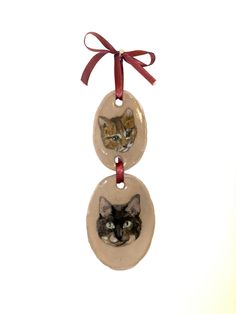 two cats hanging from a red ribbon on top of a christmas ornament that is attached to a white wall