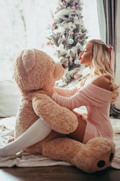 a woman sitting on the floor with a teddy bear in front of a christmas tree