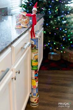 Take Elf on the Shelf to new heights. Elf on the Shelf Standing on Cans. Your Scout Elf can go anywhere by standing on cans. In this Elf idea, Elf got into the Kitchen Christmas cookies jar. New Elf on the Shelf ideas daily plus free Elf on the Shelf printables. #FrugalCouponLiving #ElfontheShelf #ElfontheShelfIdeas #ElfIdeas #funnyelfideas #funnyelfontheshelf #elfprintables #freeelfprintables #printables #freeprintables #ElfonaShelf #cans #cannedgoods #elfontheshelfhacks #elftricks #elftips Elves On A Shelf Ideas, Christmas Elves Ideas, Easy Elf On The Shelf Ideas Kitchen, Elf On The Shelf Climbing, Lazy Elf On The Shelf Ideas, Diy Elf On The Shelf Ideas, Elf On The Shelf Diy, Elves Ideas, Elf On The Shelf Printables