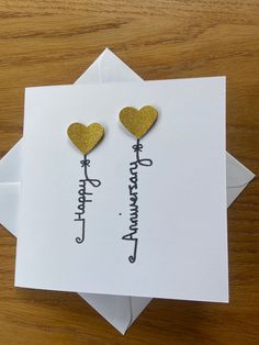 two heart shaped earrings on top of a card with the words happy anniversary written in cursive writing