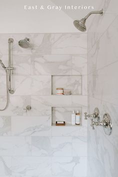 a bathroom with white marble walls and floor, shower head, shelves on the wall