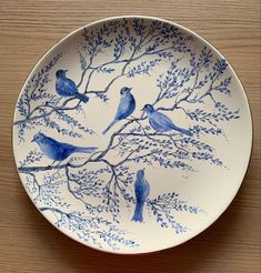 a blue and white plate with birds sitting on the tree branches in front of it