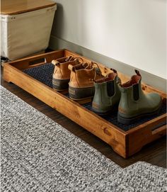 four pairs of boots are lined up in a wooden tray on the floor next to a rug