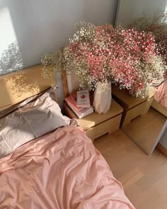 a bedroom with pink bedding and flowers in vases on the nightstand next to it