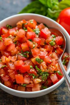 a white bowl filled with chopped tomatoes and garnished with green herbs on top