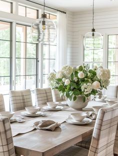 a dining room table with white flowers in a vase on top of it and chairs around the table