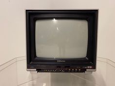 an old tv sitting on top of a glass shelf in a room with white walls